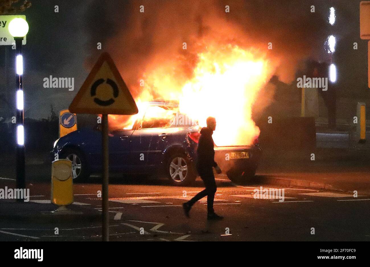Un homme passe devant une voiture en feu qui a été piratée par les Loyalistes au rond-point de Cloughfern à Newtownabbabbabbabbabbatiale. Des hommes masqués ont lancé des bombes à essence et des voitures piratées dans la zone de fidélisation au nord de Belfast. Date de la photo: Samedi 3 avril 2021. Banque D'Images