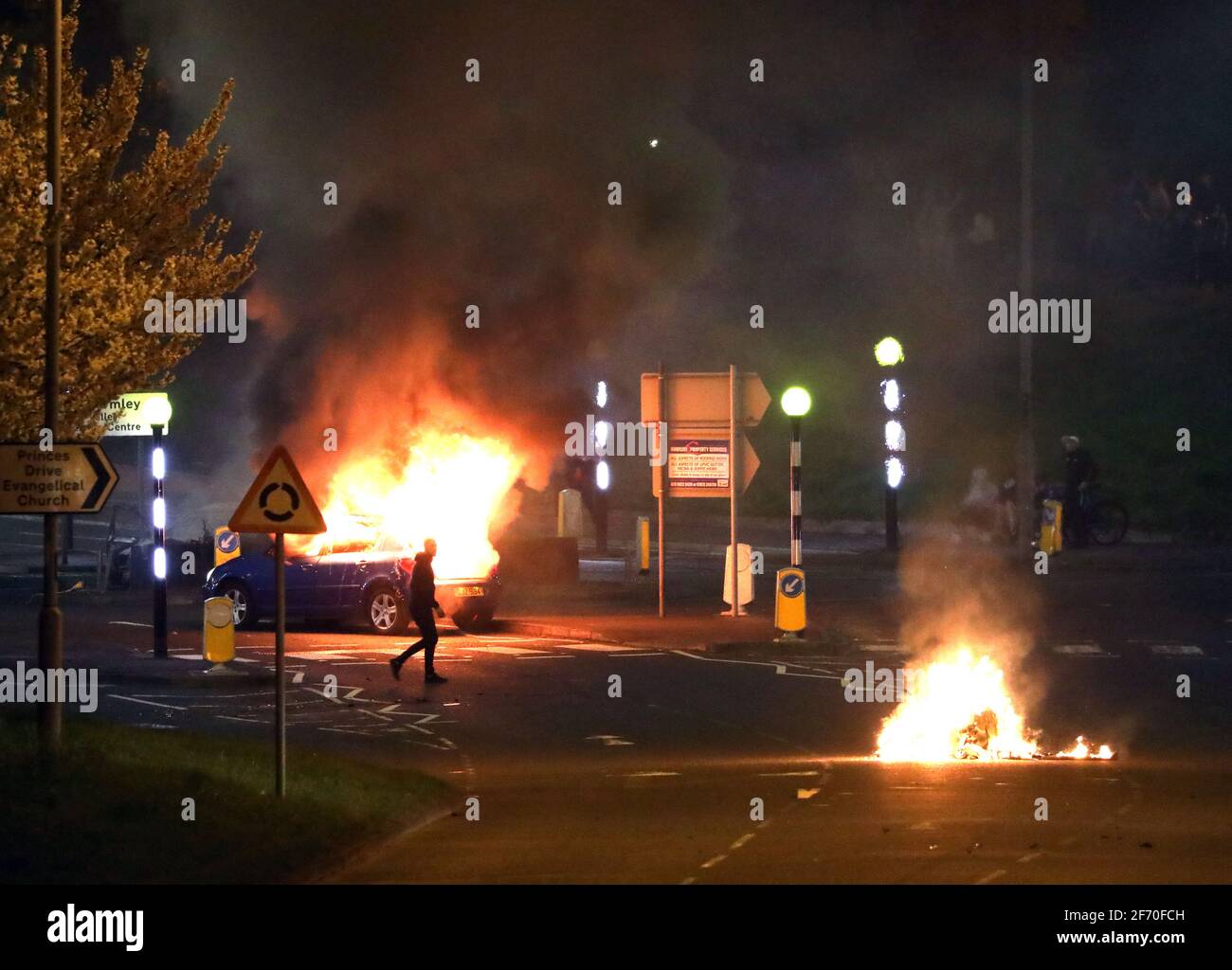 Un homme passe devant une voiture en feu qui a été piratée par les Loyalistes au rond-point de Cloughfern à Newtownabbabbabbabbabbatiale. Des hommes masqués ont lancé des bombes à essence et des voitures piratées dans la zone de fidélisation au nord de Belfast. Date de la photo: Samedi 3 avril 2021. Banque D'Images