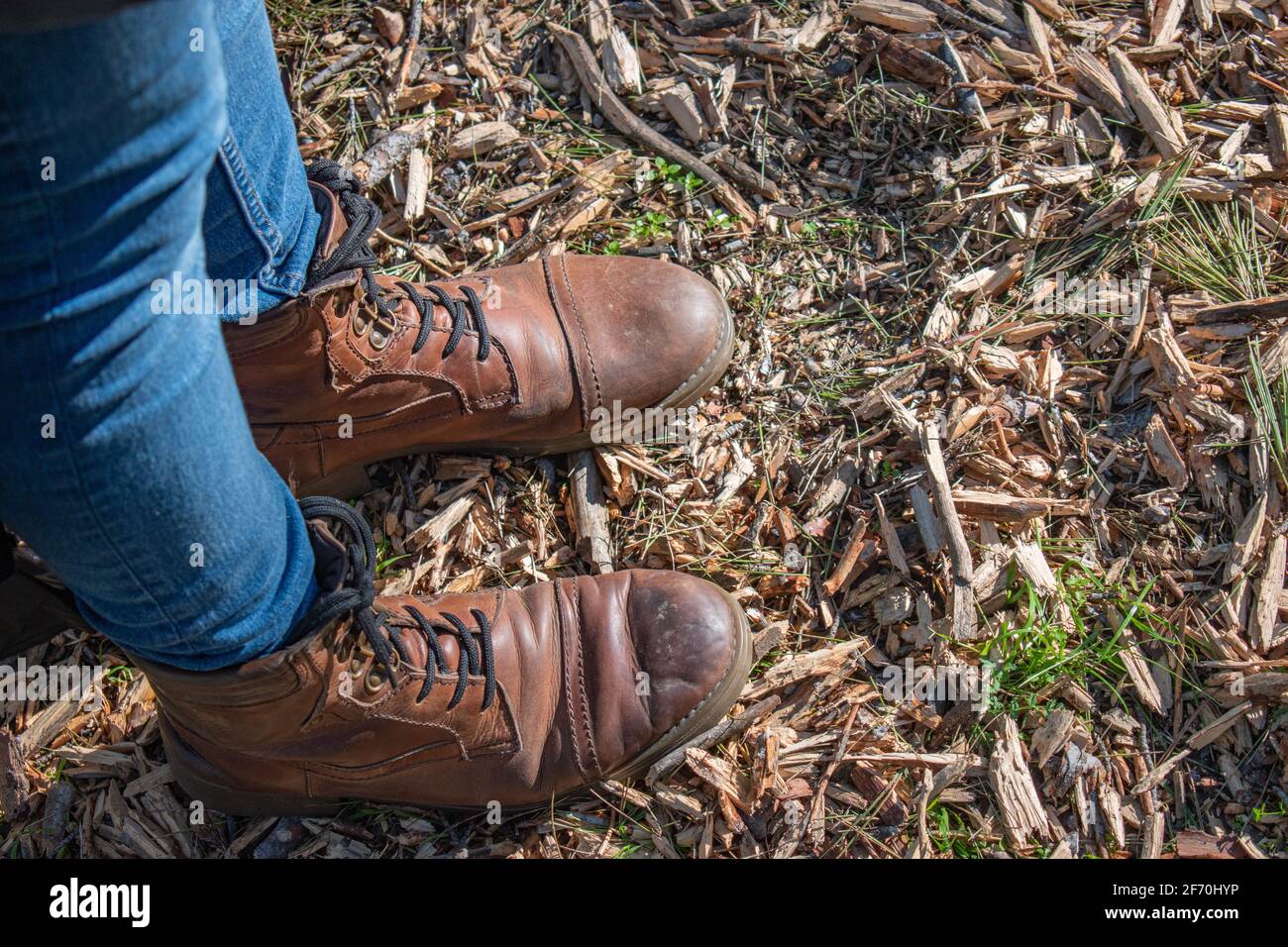 homme vêtu de jeans bleus et de bottes en cuir marron debout sur des morceaux de bois et des éclats. Gros plan. Vue de dessus. Banque D'Images