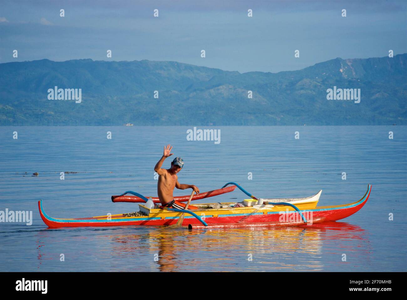 Pêcheur philippin agitant alors qu'il se prépare à prendre son canot de stabilisateur pour pêcher dans la mer de Visayan au large de Moalboal, île de Cebu, Philippines. Banque D'Images