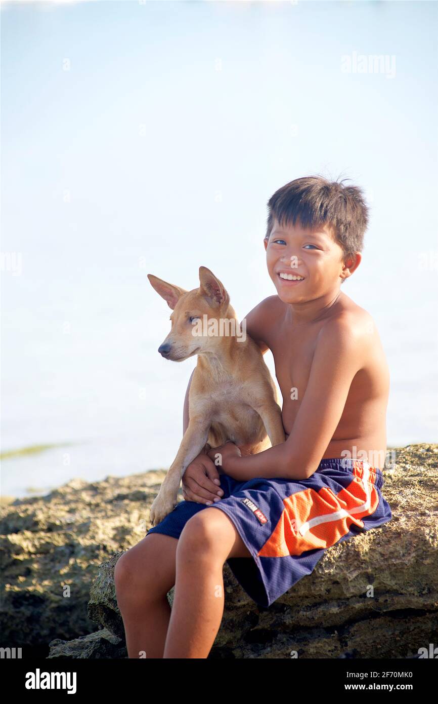 Portrait d'un garçon philippin avec un chien assis sur un rocher, Moalboal, île de Cebu, Philippines. Banque D'Images