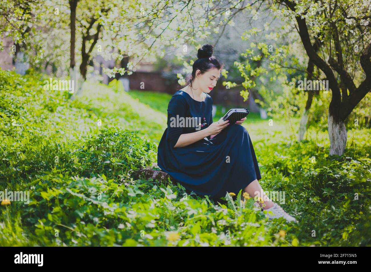 Femme heureuse assise dans le jardin de cerisier de printemps Banque D'Images