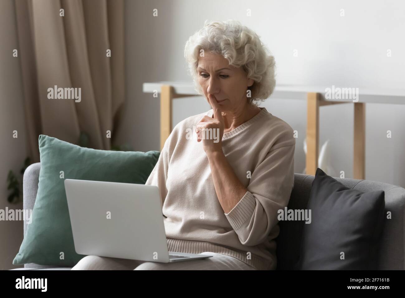 Femme âgée sérieuse utilisant un ordinateur portable pour les appels vidéo depuis la maison Banque D'Images