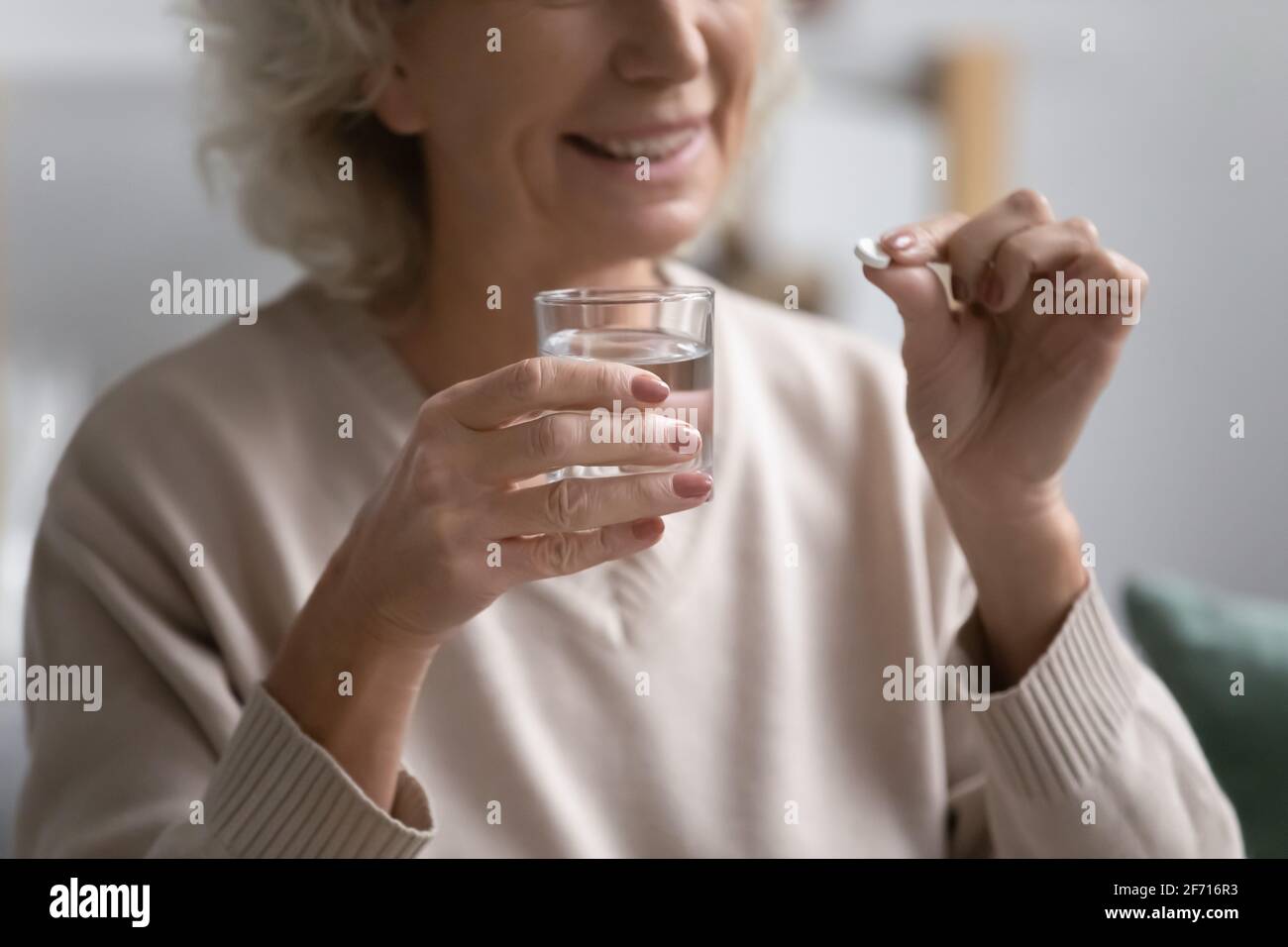 Femme âgée souriante tenant une pilule et un verre d'eau Banque D'Images