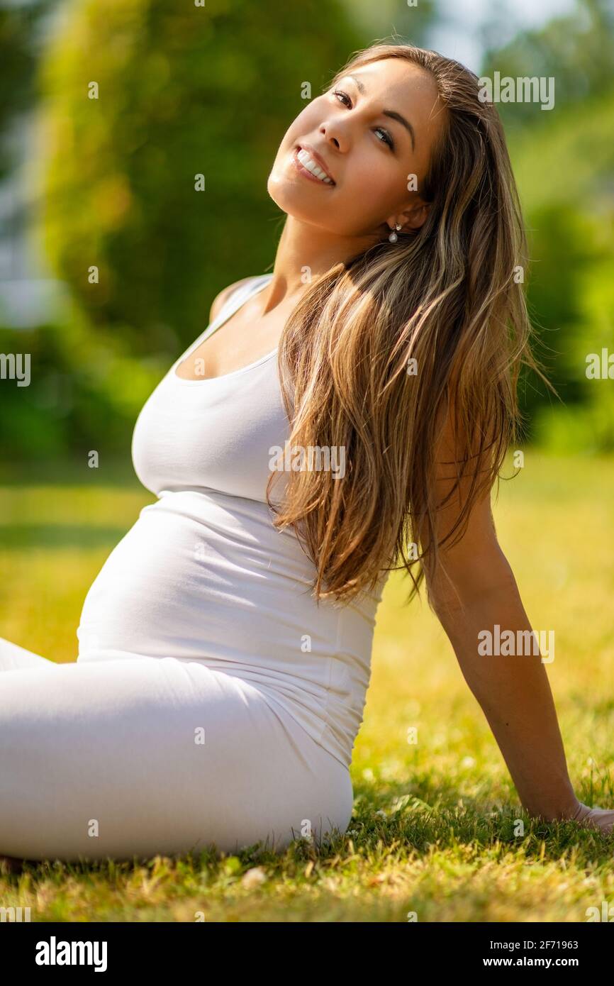 Femme enceinte gaie assise sur l'herbe dans un beau jardin Banque D'Images