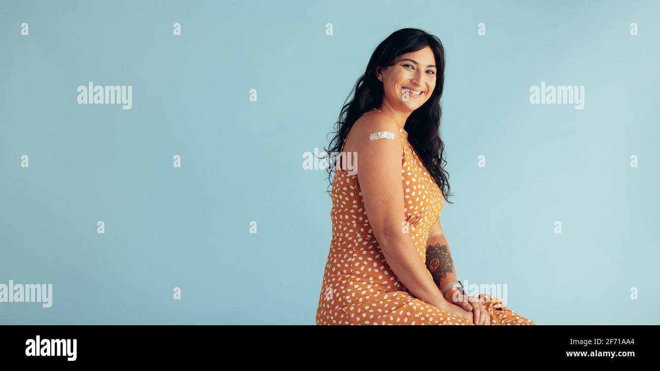 Belle femme adulte de taille moyenne avec vaccination sur son bras. Femme avec un bracelet sur son bras après avoir reçu un vaccin contre la grippe sur fond bleu. Banque D'Images Belle femme adulte de taille moyenne avec vaccination sur son bras. Femme avec un bracelet sur son bras après avoir reçu un vaccin contre la grippe sur fond bleu. Banque D'Images