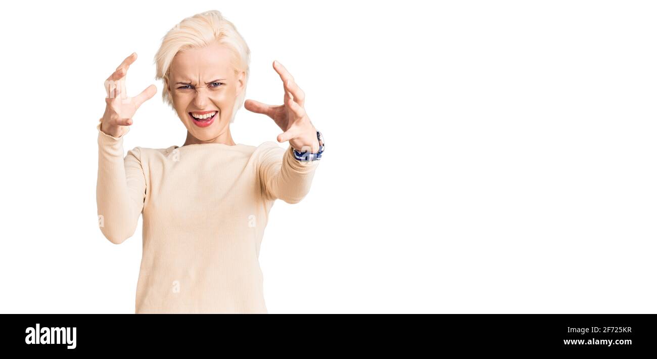 Jeune femme blonde portant des vêtements décontractés criant frustré par la rage, les mains essayant de étrangler, hurlant fou Banque D'Images