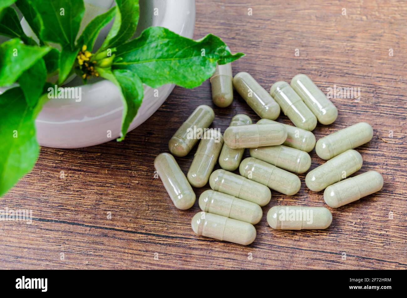 Pile de plantes médicinales en capsules et mortier céramique avec feuille verte sur fond de bois. Banque D'Images