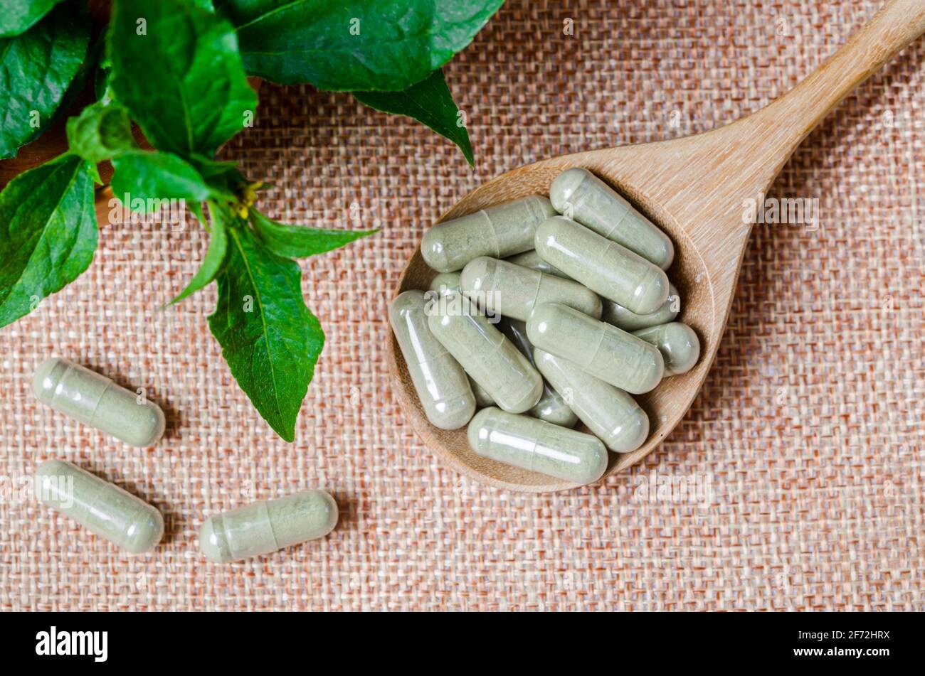 Pile de capsules de phytothérapie dans une cuillère en bois avec une feuille verte sur fond de sac. Banque D'Images