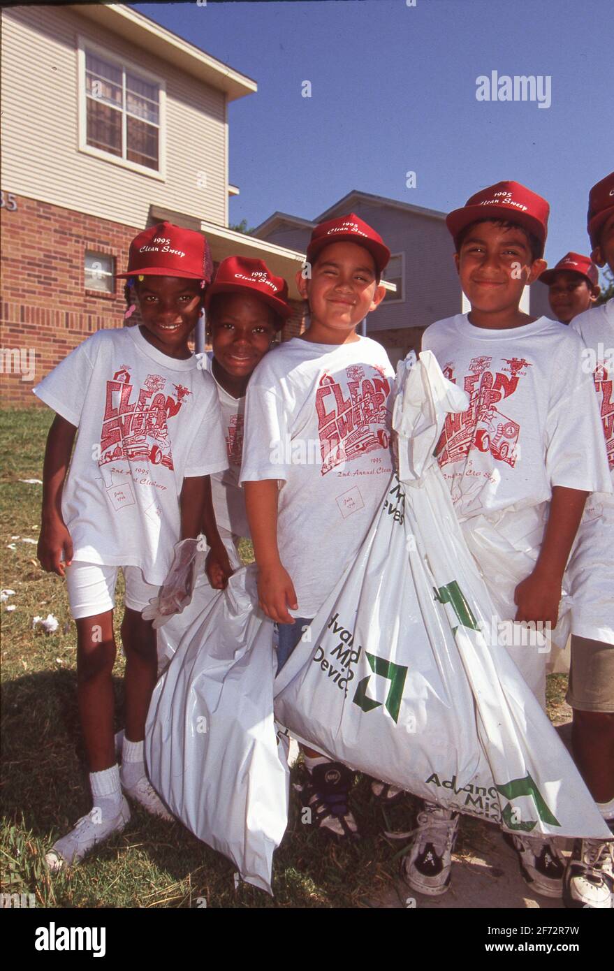Austin, TX États-Unis: Les enfants hispaniques et noirs remplissent des sacs de déchets lors d'un effort volontaire pour nettoyer les terrains d'un projet de logement à faible revenu. ©Bob Daemmrich Banque D'Images
