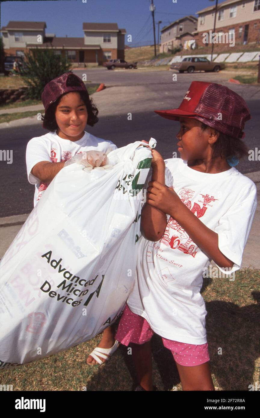Les filles d'école moyenne hispanique et noire remplissent un sac de déchets lors d'un effort bénévole pour nettoyer les terrains d'un projet de logement à faible revenu, Austin TX. 1995 Banque D'Images