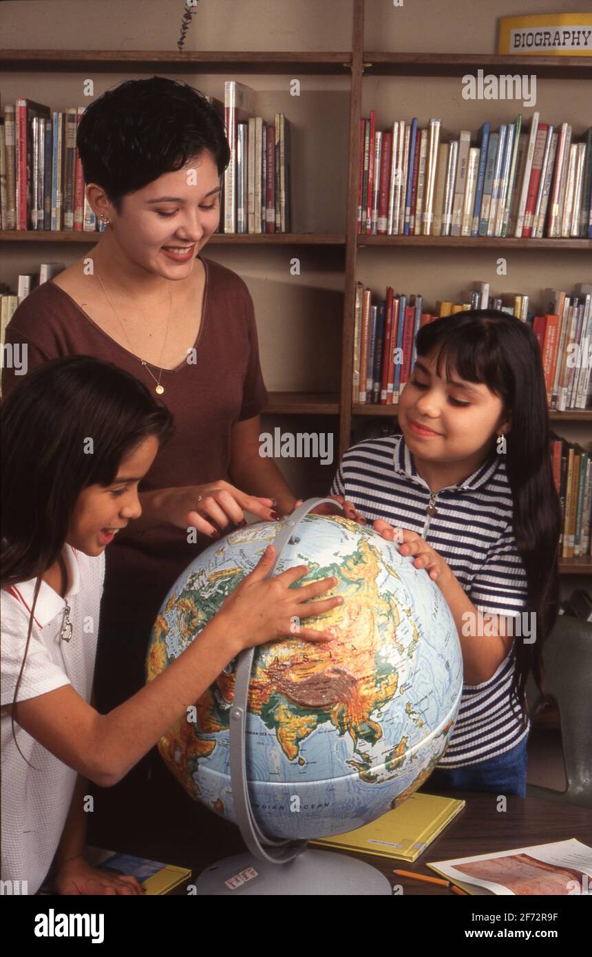Une adolescente hispanique utilise globe pour enseigner aux élèves de 5e année la géographie dans la bibliothèque scolaire Austin TX. 1996 Banque D'Images