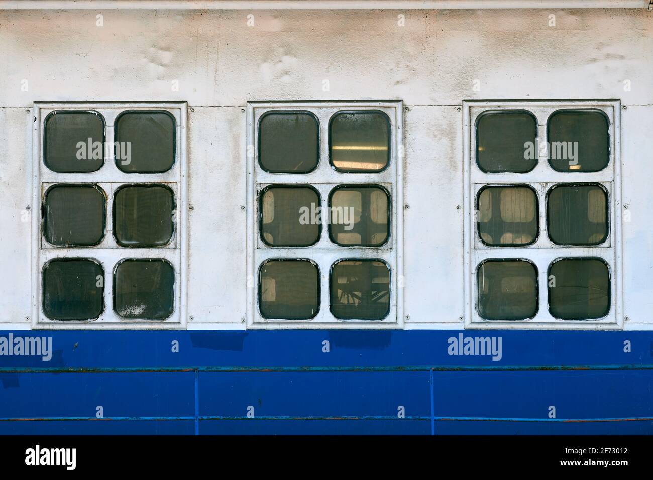 Vitres et prises d'air de la cabine sur le côté extérieur du navire. Gros plan sur la coque du paquebot d'époque. Anciennes fenêtres de cabine de bateau, murs blanc et bleu. Banque D'Images