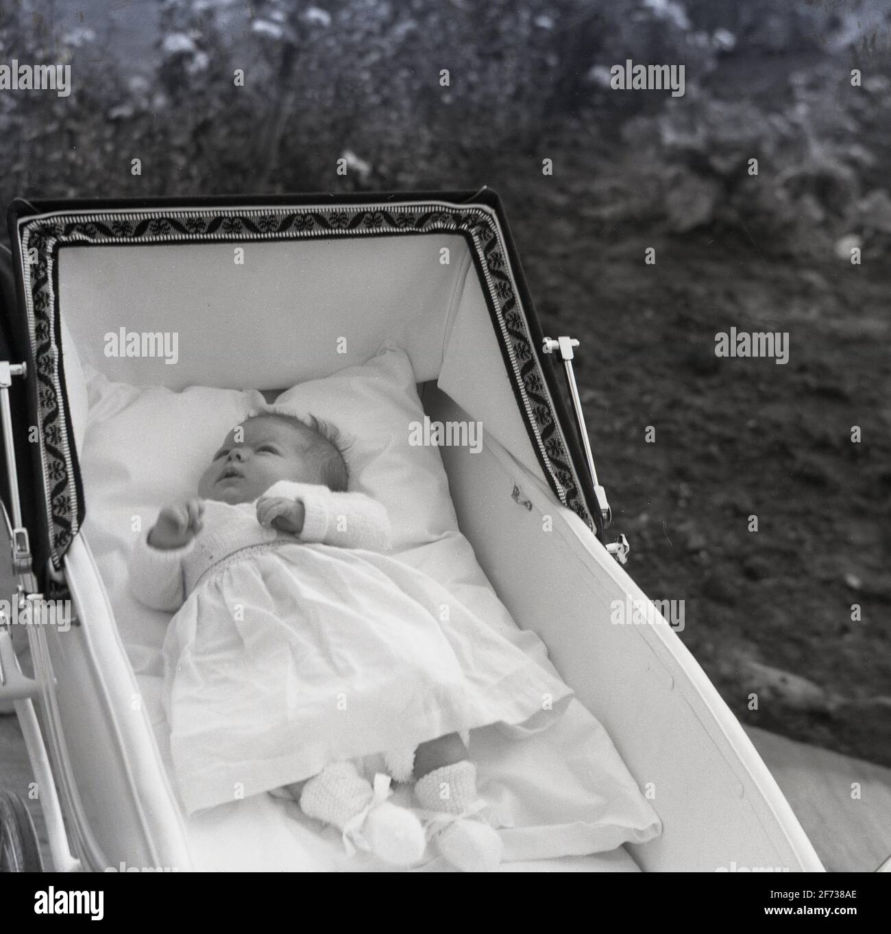 1958, historique, à l'extérieur, dans un landau ou un babycalèche construit en autocar de l'époque, un nouveau-né allongé sur son dos se repose. Pour une respiration optimale et pour obtenir tout l'oxygène dont ils ont besoin, les nouveaux bébés doivent être à plat et le pram classique construit en autocar avec sa grande capuche, son cadre généreux et son intérieur entièrement plat leur permettent de faire cela avec beaucoup d'espace. Cette position allongée favorise également le développement correct de la colonne vertébrale et des hanches d'un bébé. Banque D'Images