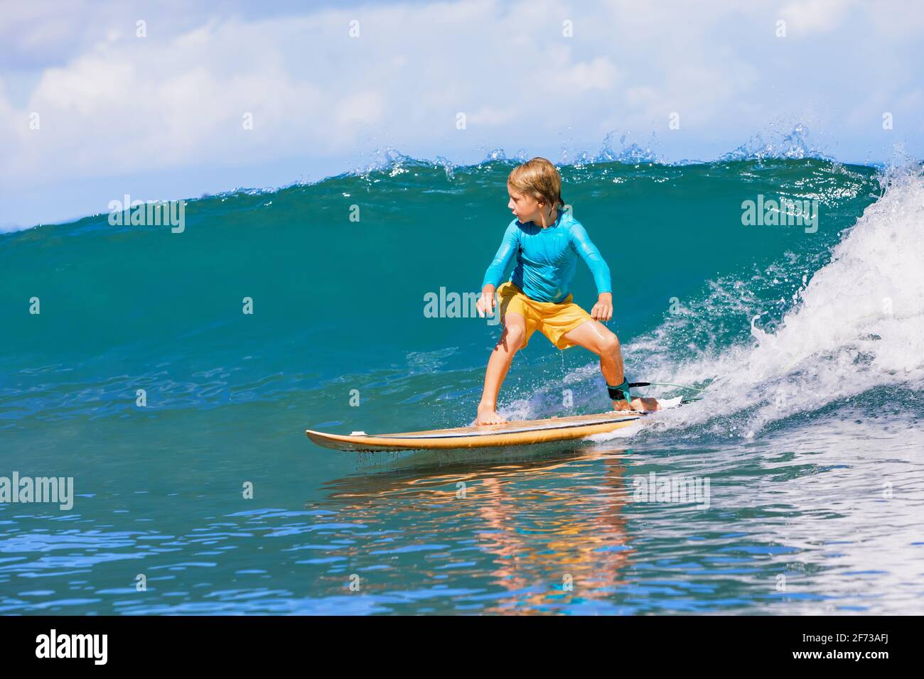 Joyeux garçon de surf - jeune surfeur apprendre à monter à bord de surf avec plaisir sur les vagues de mer. Mode de vie actif en famille, leçons de sports nautiques en plein air pour les enfants. Banque D'Images