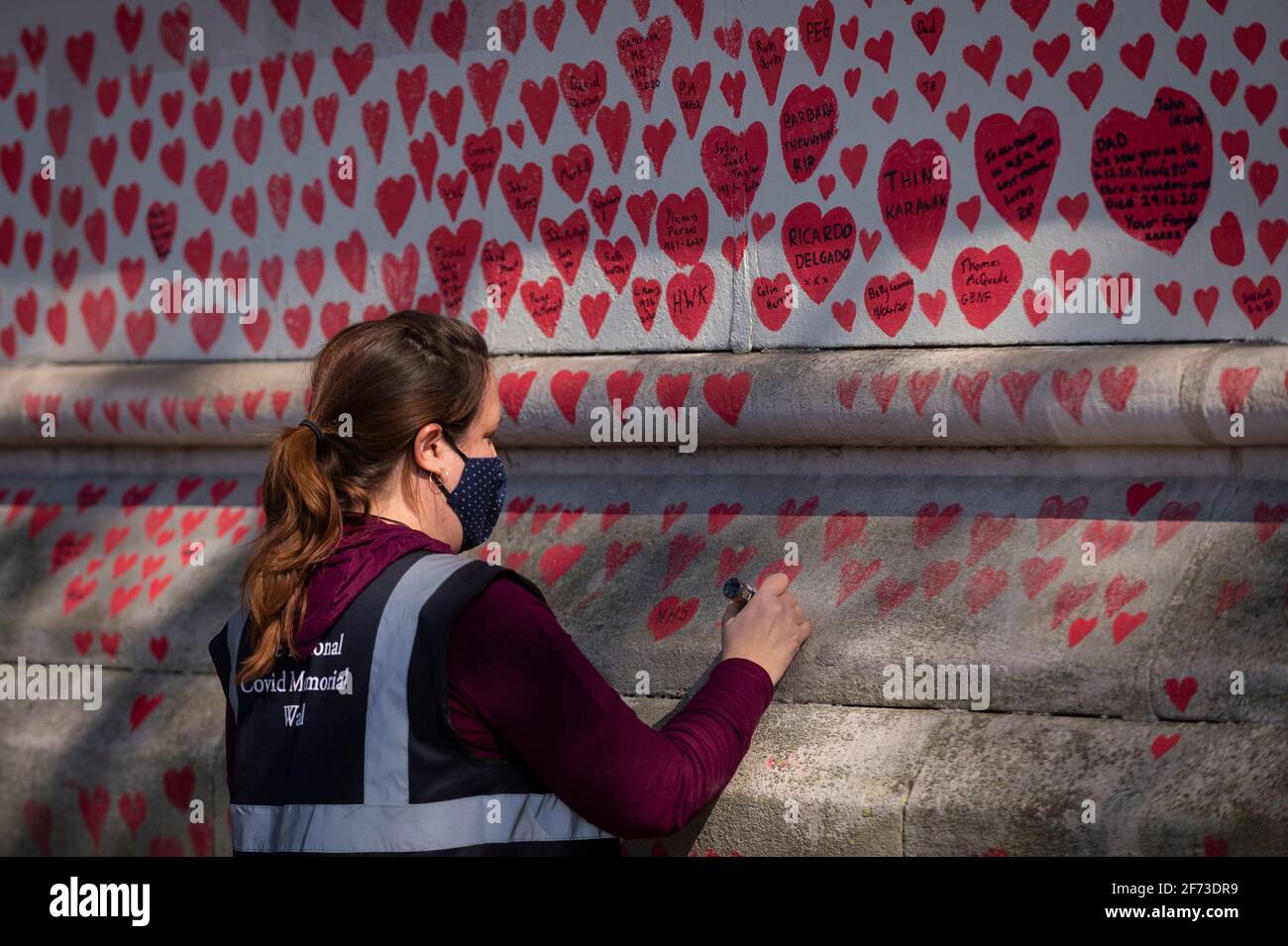 Londres, Royaume-Uni. 4 avril 2021. Un volontaire tire les coeurs le dimanche de Pâques sur un mur à Lambeth près de la Tamise, chaque cœur représentant une personne décédée pendant la pandémie de coronavirus au Royaume-Uni. Appelé le mur commémoratif national Covid, il a été créé par le groupe Covid-19 Bereaved Families for Justice avec des travaux qui débutent il y a une semaine et s'étendra sur un demi-mile à la fin. Credit: Stephen Chung / Alamy Live News Banque D'Images