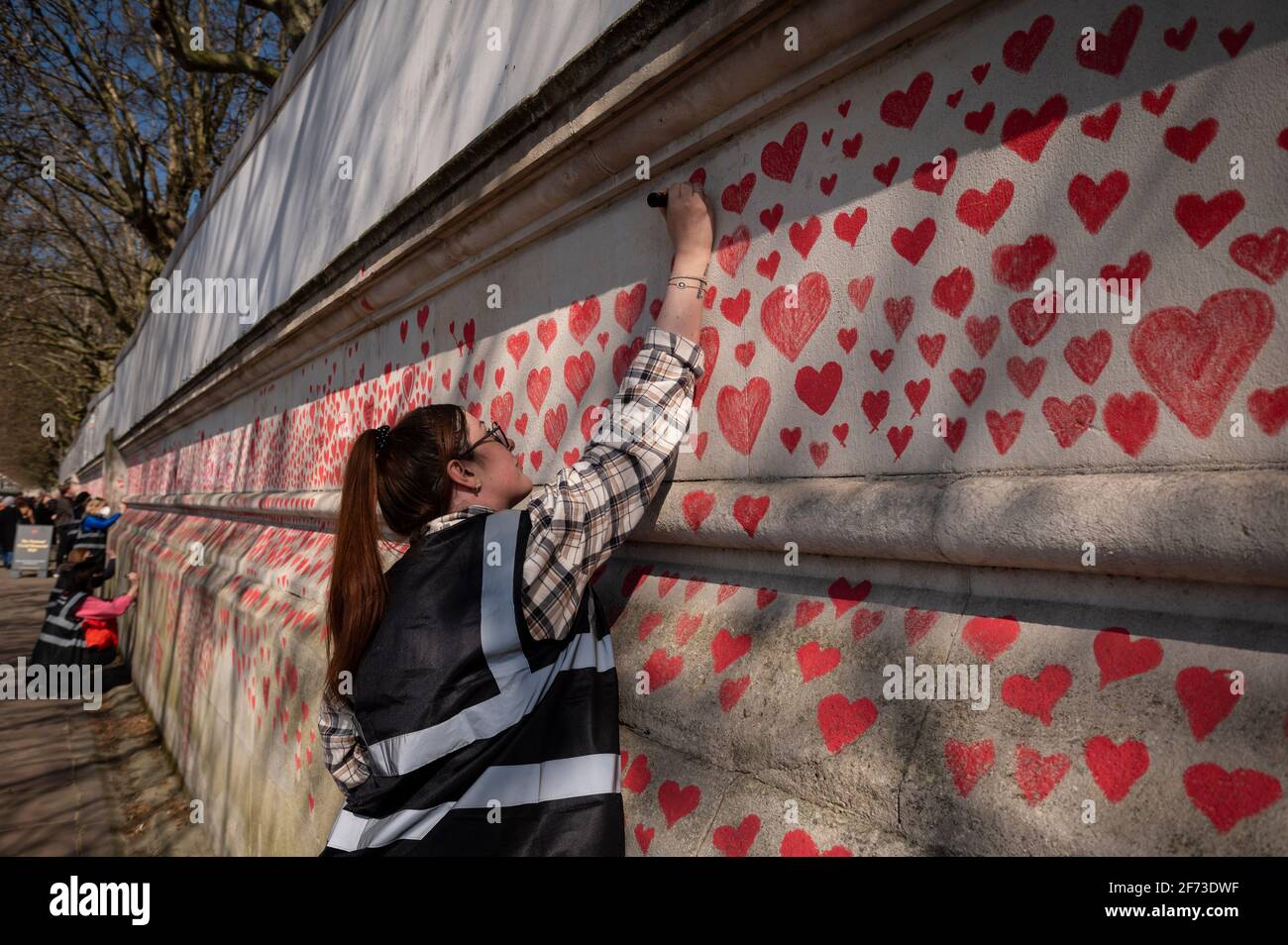 Londres, Royaume-Uni. 4 avril 2021. Un volontaire tire les coeurs le dimanche de Pâques sur un mur à Lambeth près de la Tamise, chaque cœur représentant une personne décédée pendant la pandémie de coronavirus au Royaume-Uni. Appelé le mur commémoratif national Covid, il a été créé par le groupe Covid-19 Bereaved Families for Justice avec des travaux qui débutent il y a une semaine et s'étendra sur un demi-mile à la fin. Credit: Stephen Chung / Alamy Live News Banque D'Images