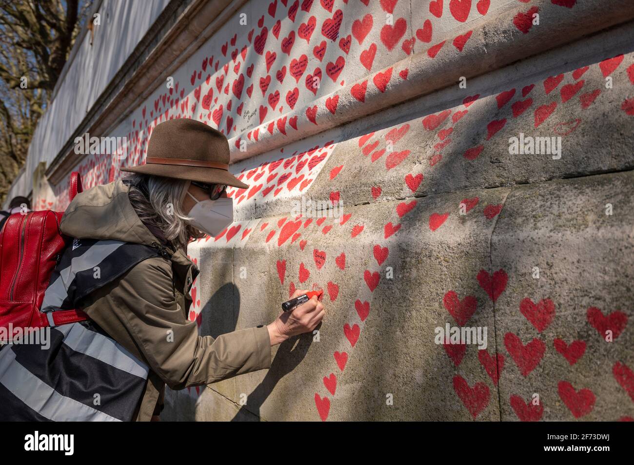 Londres, Royaume-Uni. 4 avril 2021. Un volontaire tire les coeurs le dimanche de Pâques sur un mur à Lambeth près de la Tamise, chaque cœur représentant une personne décédée pendant la pandémie de coronavirus au Royaume-Uni. Appelé le mur commémoratif national Covid, il a été créé par le groupe Covid-19 Bereaved Families for Justice avec des travaux qui débutent il y a une semaine et s'étendra sur un demi-mile à la fin. Credit: Stephen Chung / Alamy Live News Banque D'Images