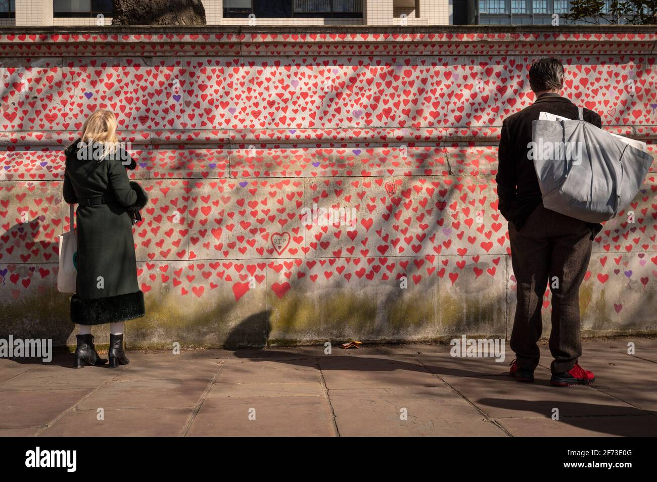 Londres, Royaume-Uni. 4 avril 2021. Un couple regarde les coeurs le dimanche de Pâques sur un mur à Lambeth près de la Tamise, chaque cœur représentant une personne décédée pendant la pandémie de coronavirus au Royaume-Uni. Appelé le mur commémoratif national Covid, il a été créé par le groupe Covid-19 Bereaved Families for Justice avec des travaux qui débutent il y a une semaine et s'étendra sur un demi-mile à la fin. Credit: Stephen Chung / Alamy Live News Banque D'Images