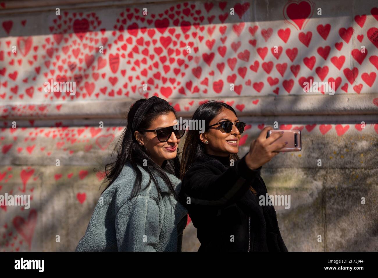 Londres, Royaume-Uni. 4 avril 2021. Les volontaires prennent un selfie contre le cœur le dimanche de Pâques sur un mur à Lambeth près de la Tamise, chaque cœur représentant une personne décédée pendant la pandémie de coronavirus au Royaume-Uni. Appelé le mur commémoratif national Covid, il a été créé par le groupe Covid-19 Bereaved Families for Justice avec des travaux qui débutent il y a une semaine et s'étendra sur un demi-mile à la fin. Credit: Stephen Chung / Alamy Live News Banque D'Images