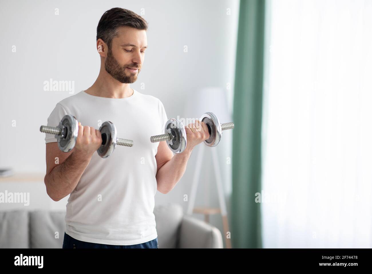 Gros plan de beau barbu homme faisant l'entraînement de haltères à la maison Banque D'Images