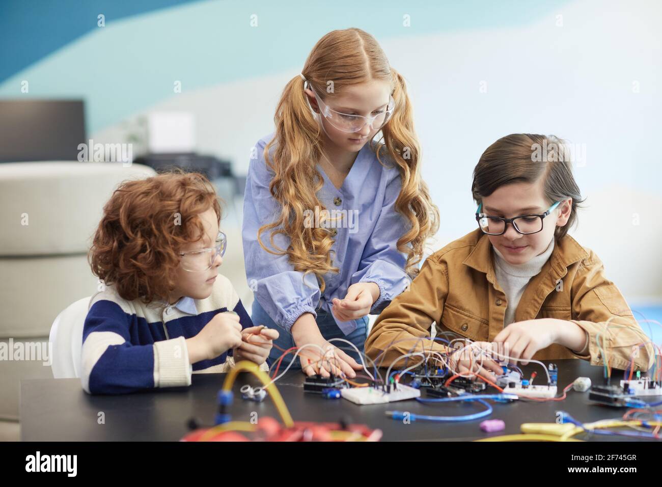 Vue de face de trois enfants construisant des robots pendant l'ingénierie classe dans l'école de développement Banque D'Images