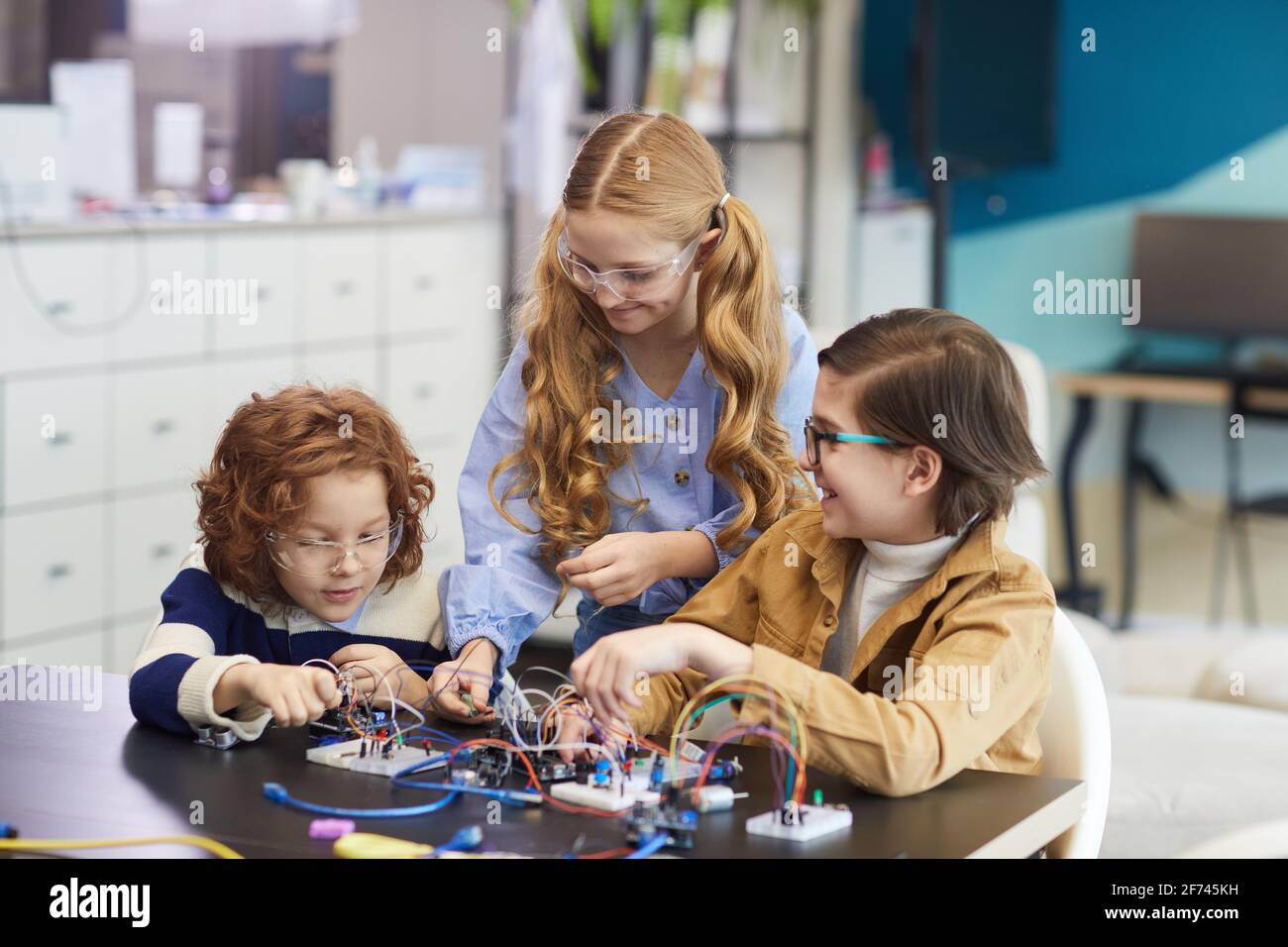 Portrait de trois enfants souriants expérimentant avec des circuits électriques pendant construction de robots en cours d'ingénierie à l'école Banque D'Images