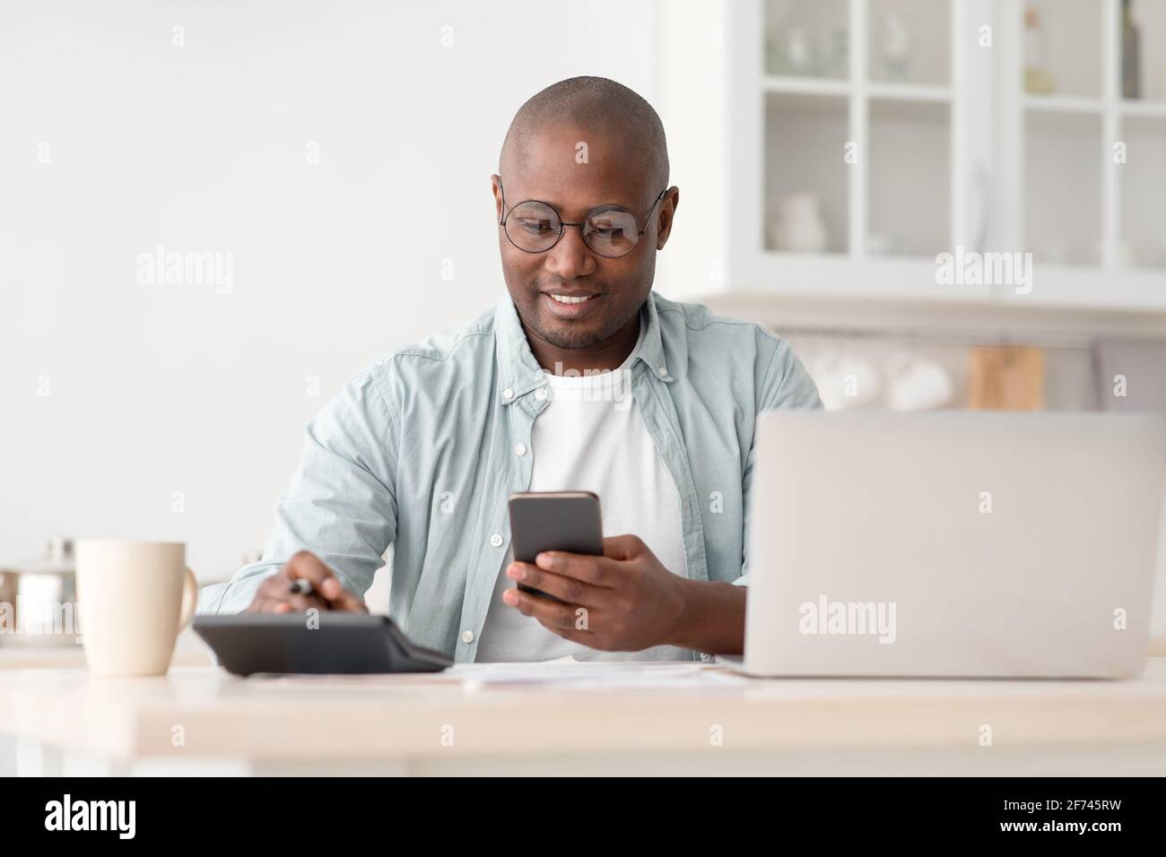 Concept d'épargne et de finances. Homme noir mature utilisant une calculatrice, un téléphone et un ordinateur portable Banque D'Images