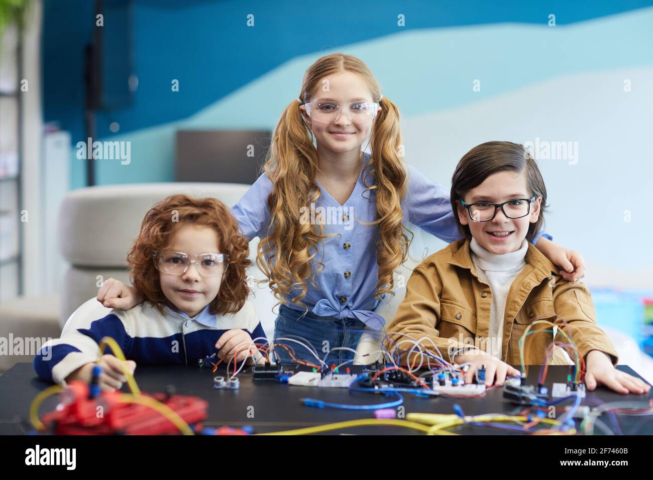 Vue de face de trois enfants construisant des robots en ingénierie classe et sourire à l'appareil photo heureusement Banque D'Images