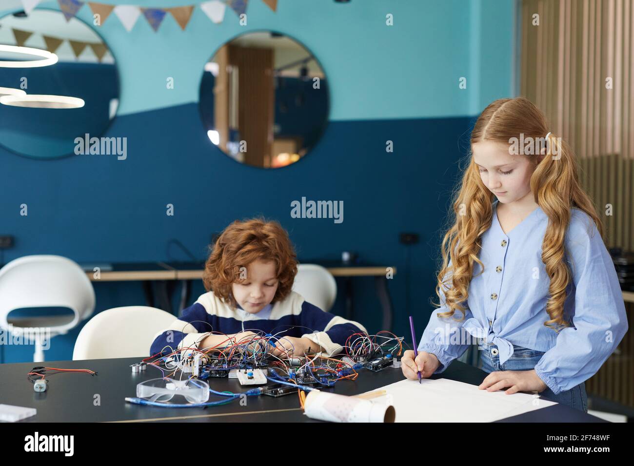Portrait des schémas de dessin de garçon et de fille tout en construisant des robots pendant la classe d'ingénierie à l'école, l'espace de copie Banque D'Images