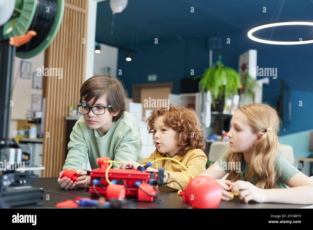 Portrait de trois enfants utilisant des robots pendant la classe d'ingénierie à l'école moderne, espace de copie Banque D'Images