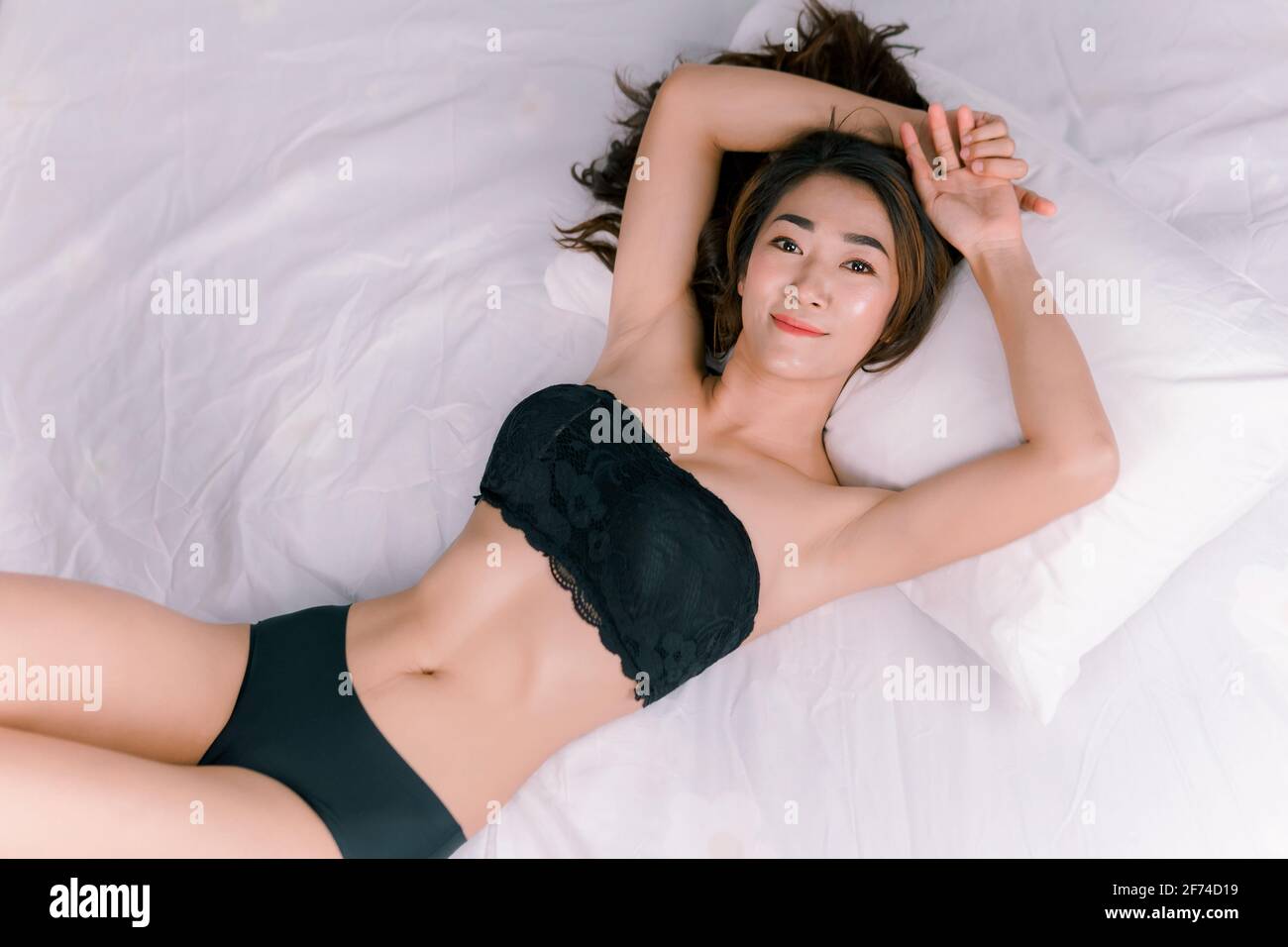 Sexy femme asiatique portant un bikini noir sur un blanc lit Banque D'Images