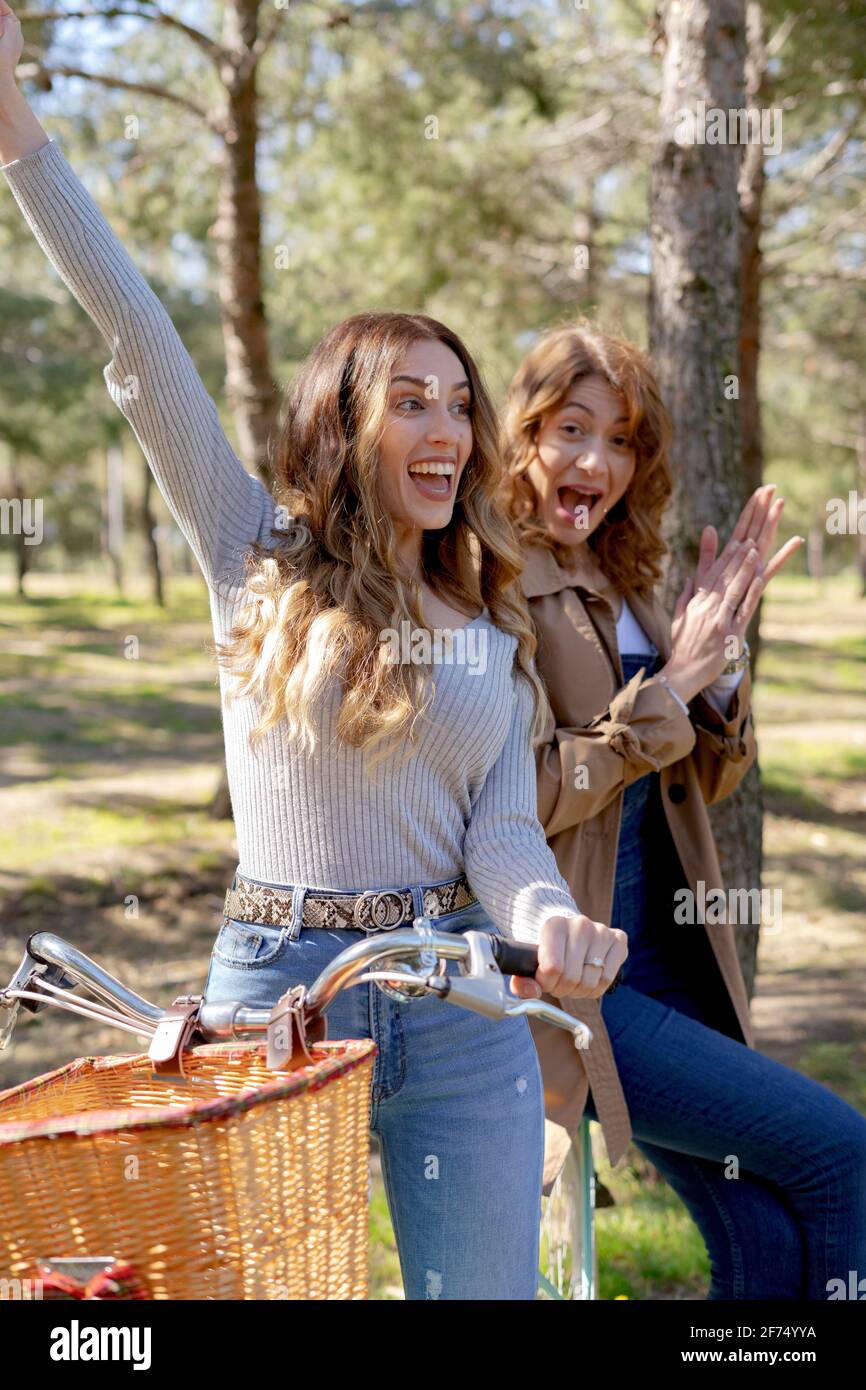 De jeunes amies souriantes et souriantes regardent l'appareil photo à vélo dans un parc ensoleillé en été Banque D'Images