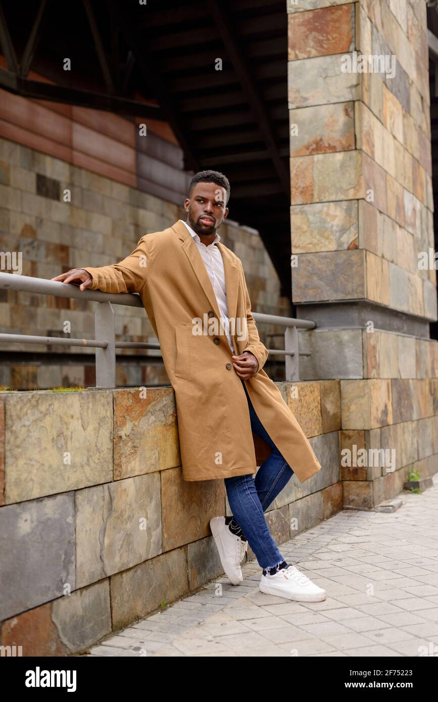 Corps complet d un homme afro americain portant un manteau tendance mur de pierre de batiment dans la ville et vue loin Photo Stock Alamy