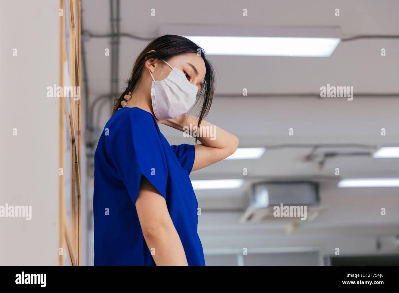 Jeune femme asiatique fatiguée et frustrée portant l'uniforme et masque chirurgical souffrant de douleurs au cou pendant le travail à l'hôpital au cours de l'épidémie de covid-19 Banque D'Images