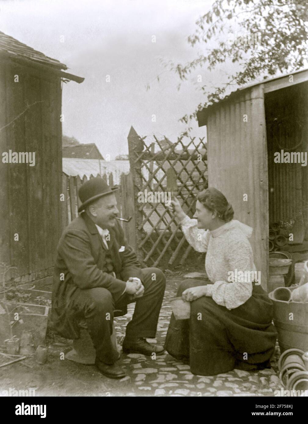 Femme et homme victorien partagent une blague derrière le hangar de potage (c. 1900) – toutefois, elle semble le menacer d'une truelle! L'emplacement est Gloucestershire, Angleterre, Royaume-Uni. Banque D'Images