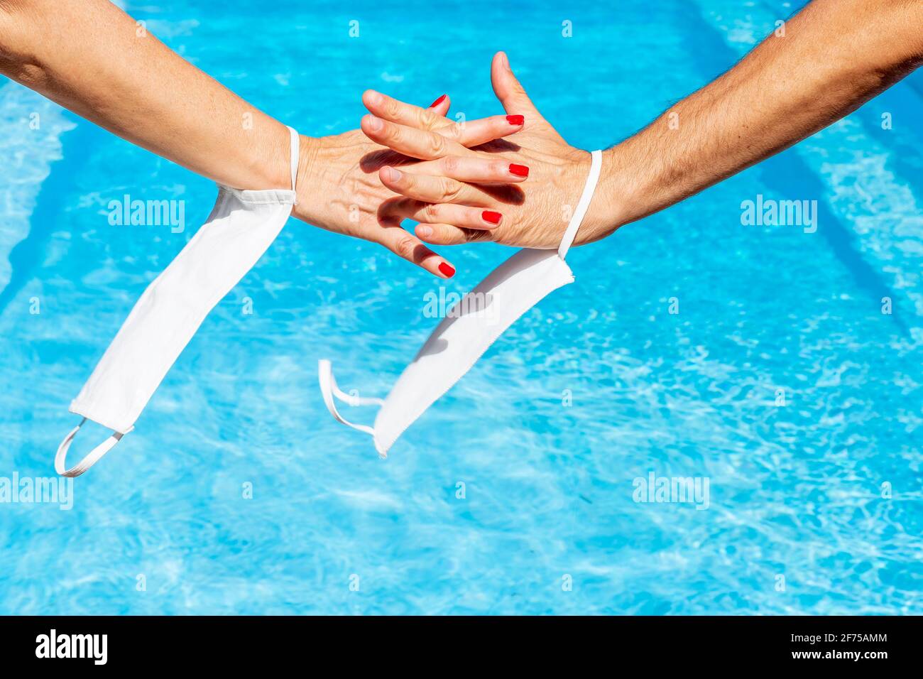Une main femelle s'entrelace avec une main mâle sur l'eau d'une piscine, avec des masques protecteurs contre le covid-19 accrochés aux poignets Banque D'Images