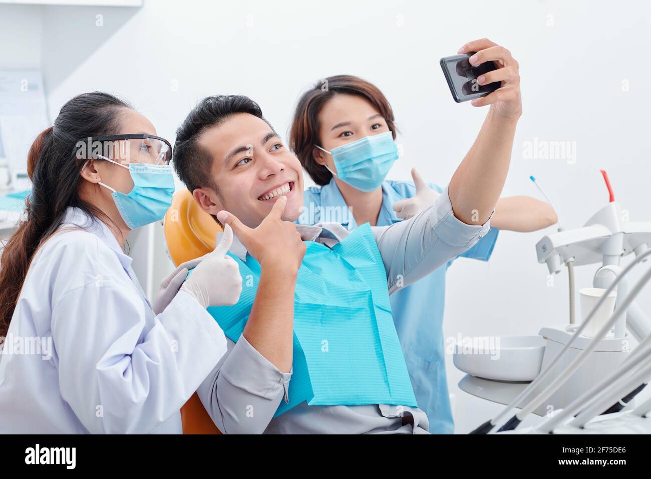 Jeune homme asiatique heureux avec son nouveau sourire prenant selfie avec dentiste et son assistant pour les médias sociaux Banque D'Images