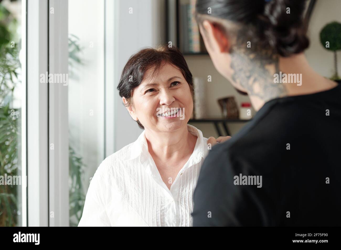 Bonne femme mûre souriante de race mixte regardant le fils adulte visiter elle à la maison Banque D'Images