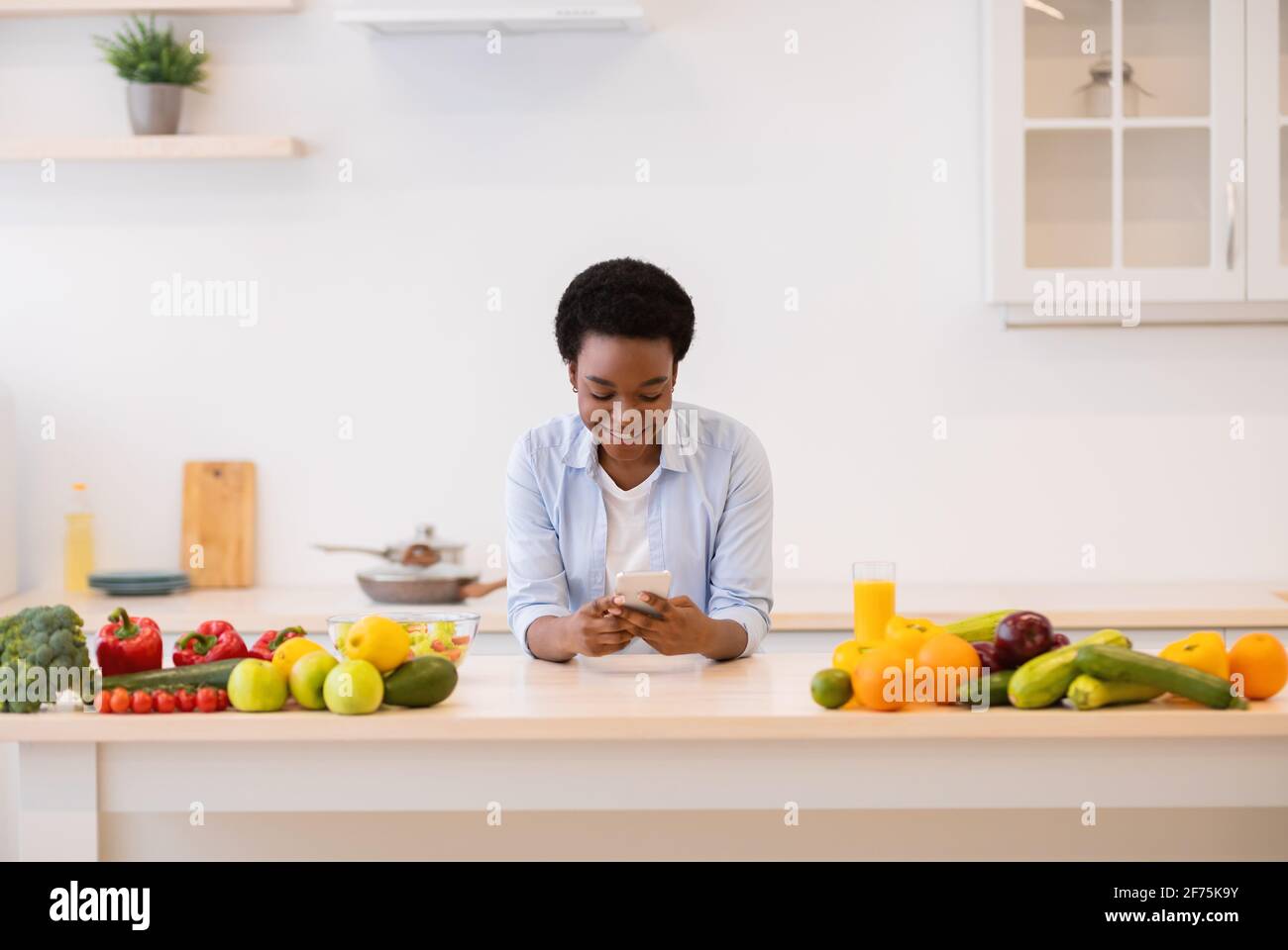 Black Lady utilisant un téléphone portable avec application de perte de poids cuisson dans la cuisine Banque D'Images