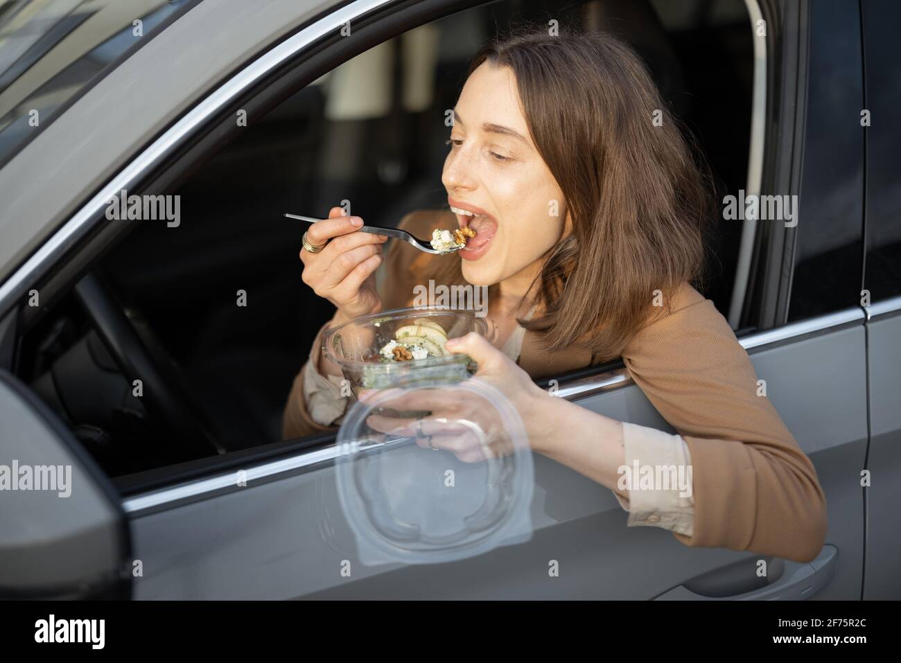 Belle femme mangeant de la salade heathy dans la voiture. Reçu une commande de nourriture à emporter. Prenez un en-cas rapide lors de la pause déjeuner. Banque D'Images