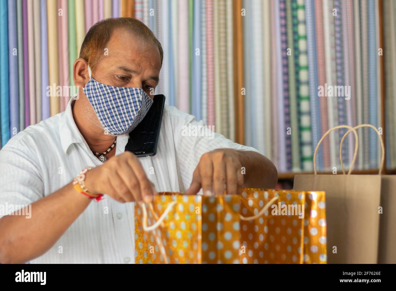 Commerçant avec masque médical vérifiant les sacs commandés avant la remise au client - concept de confirmation de commande, prenant les commandes du téléphone pendant Banque D'Images