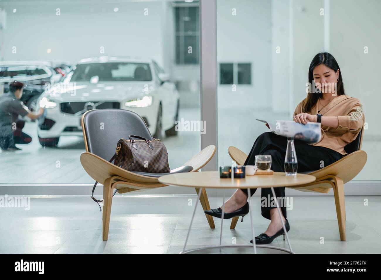 Client asiatique femme lisant et attendant mécanicien vérifier pour maintenir sa voiture dans le centre de service de maintenance avec la partie de salle d'exposition Banque D'Images