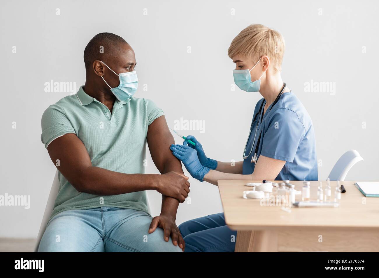 Infirmière féminine en gants et masque faisant la vaccination COVID-19 dans épaule d'un homme adulte Banque D'Images