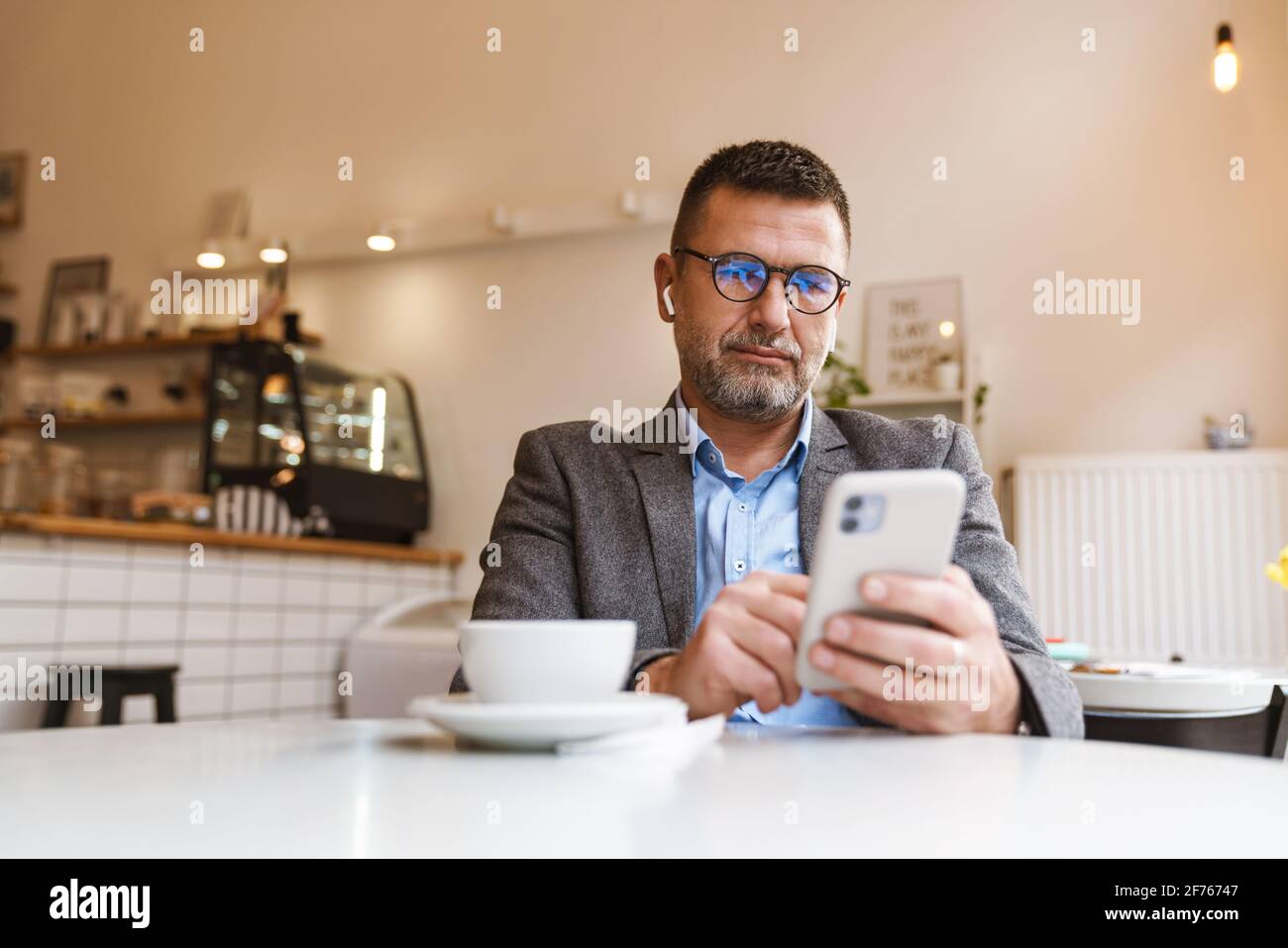 Jeune homme envoyant un message texte sur un smartphone tout en écoutant musique sur écouteurs et profiter de la connexion internet sans fil gratuite à café-restaurant Banque D'Images