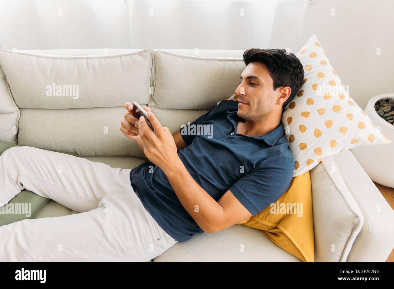 Beau jeune homme caucasien allongé sur un canapé dans un confortable permet de jouer à des jeux et de regarder des vidéos sur votre smartphone pendant la période libre temps à la maison Banque D'Images