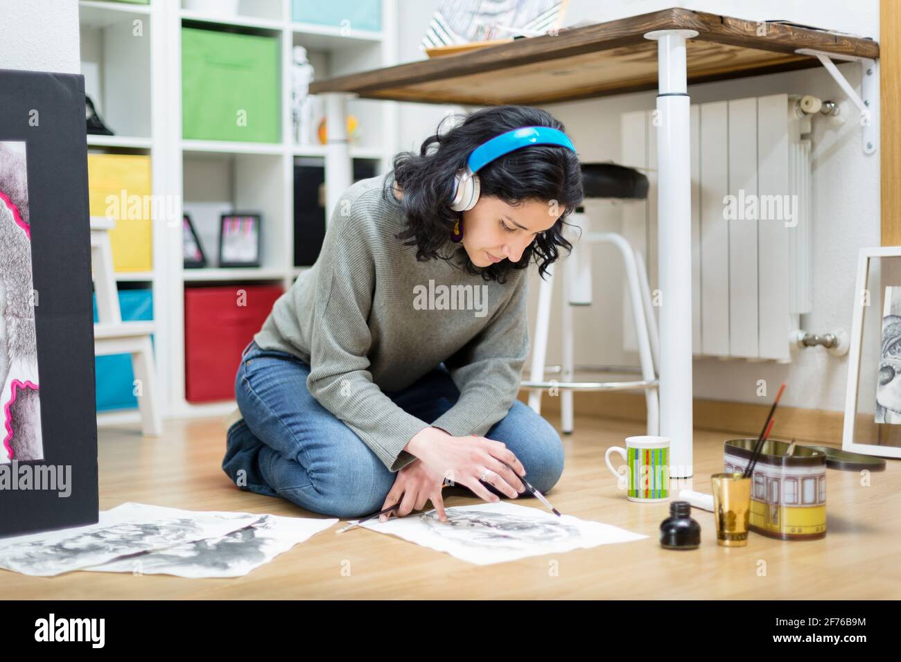Femme artiste assise sur le sol, peinture sur papier avec une brosse. Elle apprend à dessiner à la maison. Banque D'Images