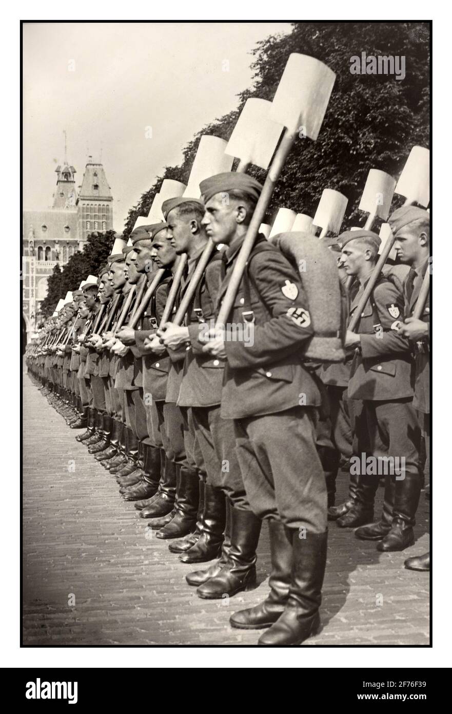 Allemagne nazie RAD Parade Reich Labor Work Service Parade uniforme avec des pelles à l'attention. Archive la deuxième Guerre mondiale des années 1940 devant le Rijksmuseum; le Service allemand du travail de Reich est mis en place pour un défilé pour Seyss Inquart.; août 4; 1940 Amsterdam Hollande le Service du travail de Reich (Reichsarbeitsdienst; RAD) était une organisation importante établie en Allemagne nazie comme une agence pour aider à atténuer les effets du chômage sur l'économie allemande, militariser la main-d'œuvre et endoctriner avec l'idéologie nazie. C'était le service officiel du travail de l'État, divisé en sections distinctes pour les hommes et les femmes. Deuxième Guerre mondiale Banque D'Images