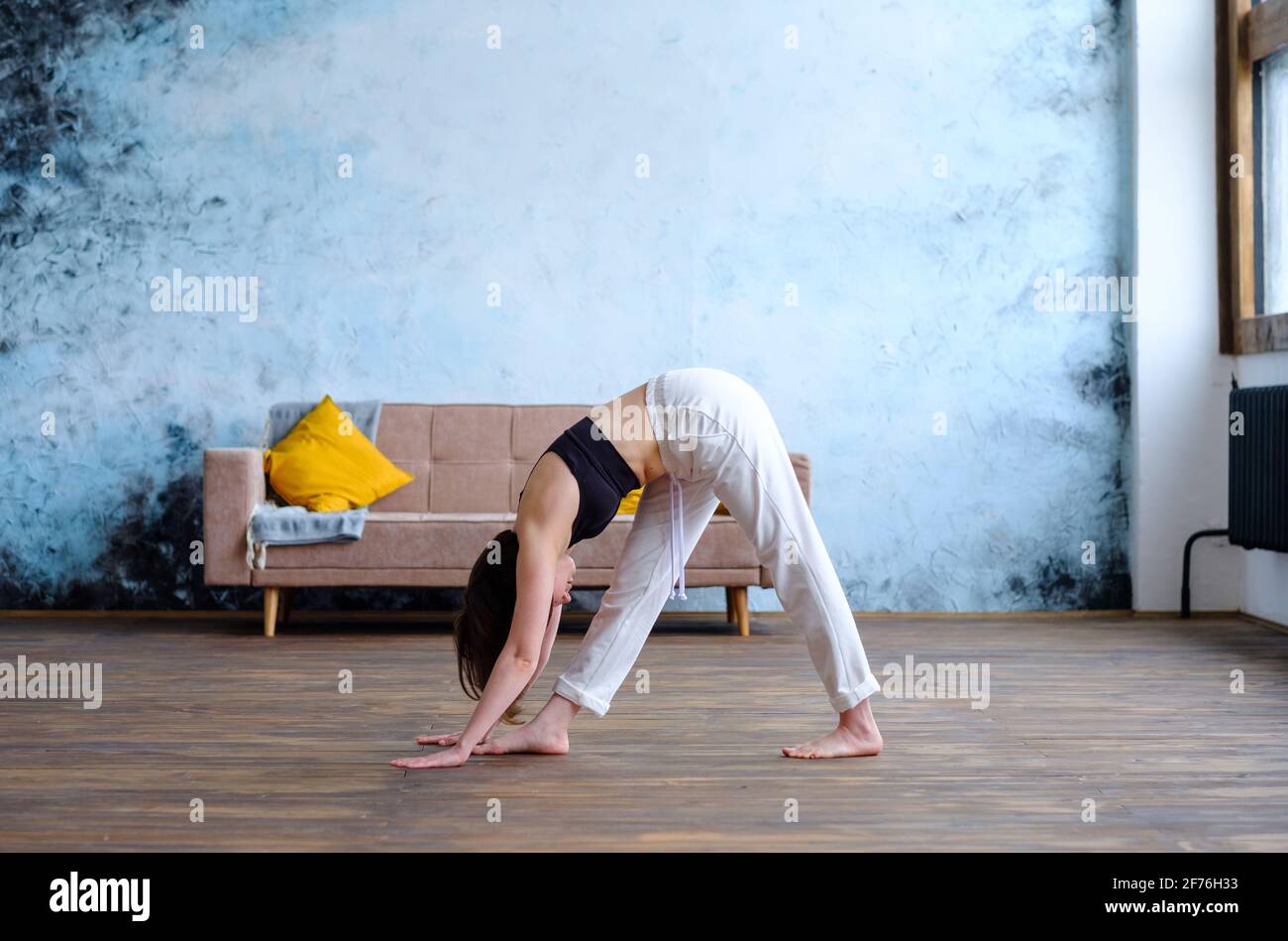 Une femme brune mignonne fait des exercices de yoga à la maison moderne à l'arrière-plan du canapé. Banque D'Images