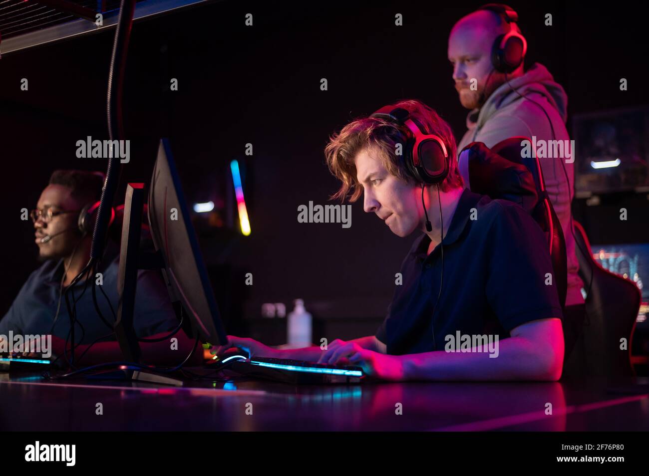 Pendant le tournoi Dota 2, deux gars de l'équipe jouent aux ordinateurs, l'entraîneur regarde de derrière. Banque D'Images